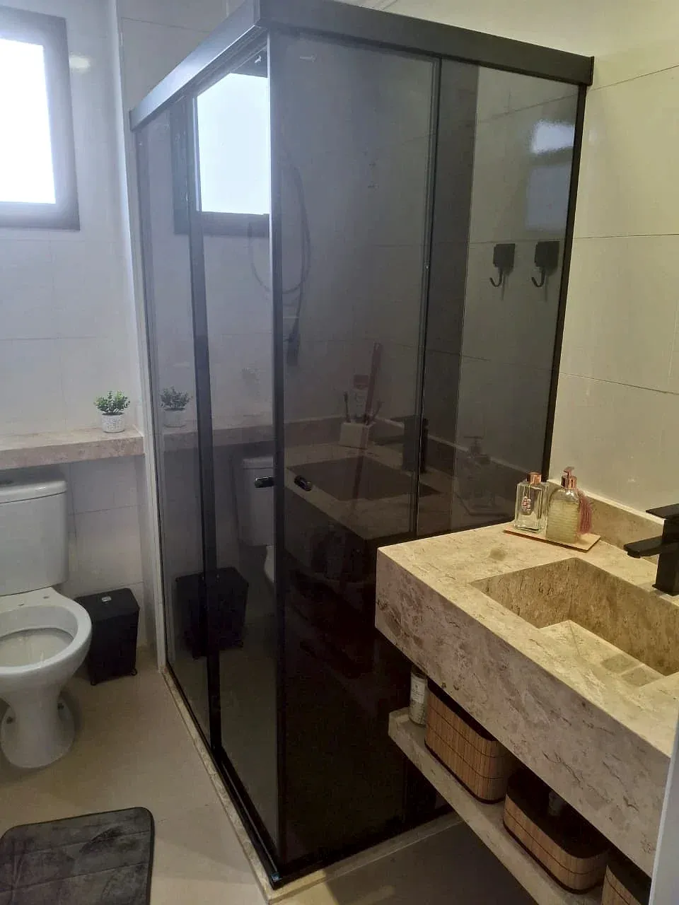 Box de canto com película fumê e perfil preto em banheiro com bancada de pedra