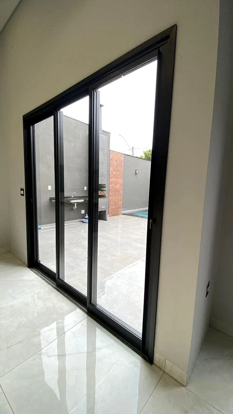 Porta de correr de três folhas em esquadria de alumínio preto, com vista para a área da piscina