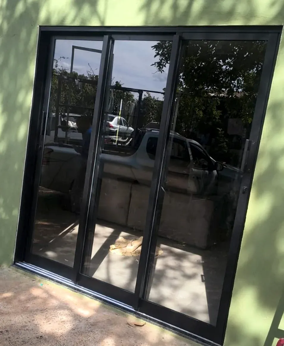 Porta de correr de três folhas em esquadria de alumínio preto em parede verde