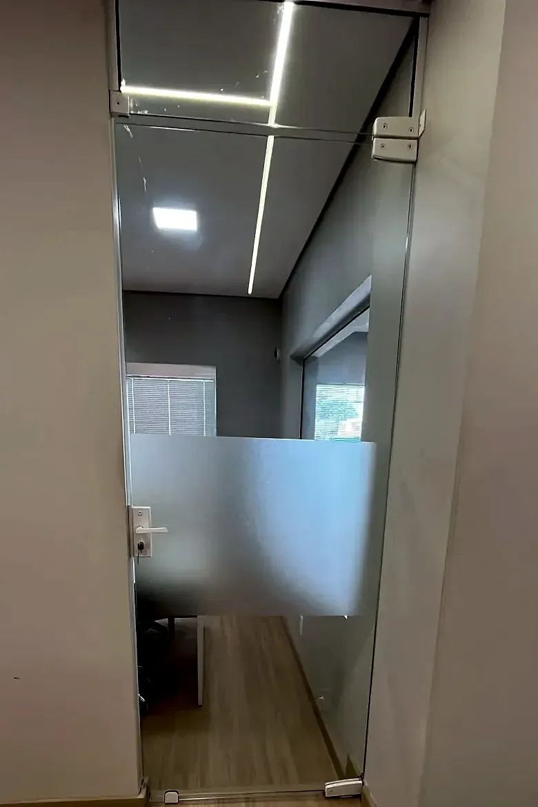 Porta de abrir em vidro temperado com faixa jateada e bandeira de vidro em escritório