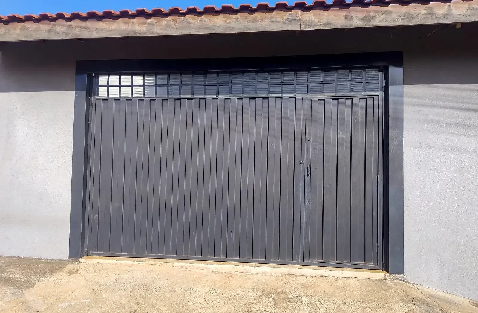 Portão de ferro preto com lambril vertical, porta social e bandeira ventilada